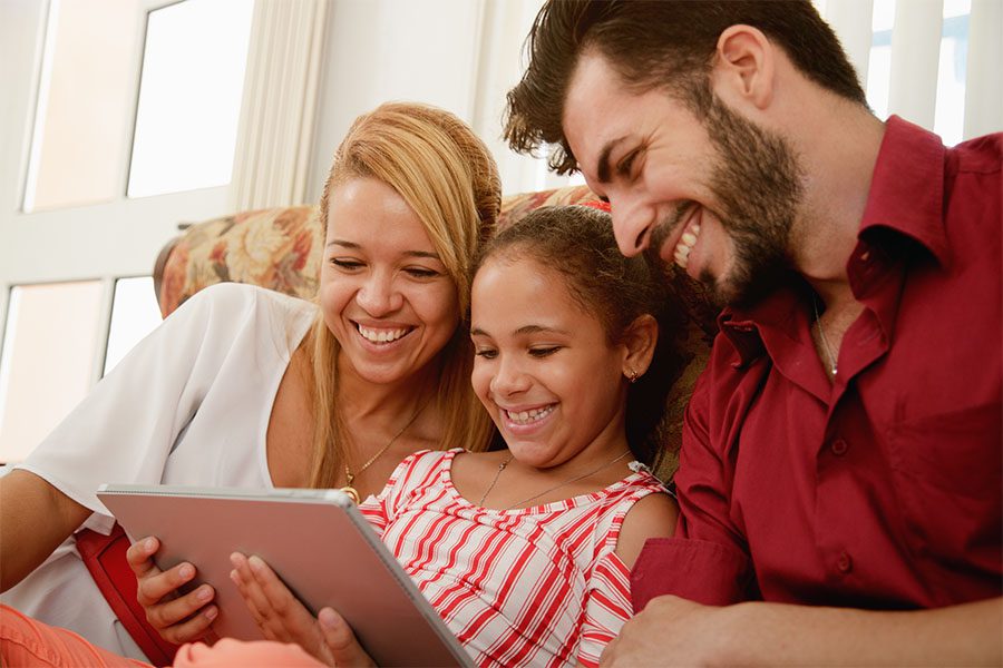 Client Center - Happy Family Sitting On Couch Using Their Tablet Together